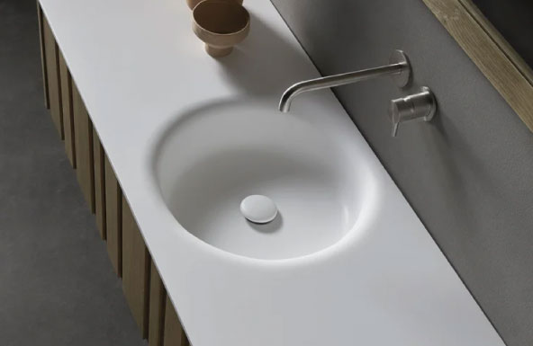 Detalle grifería plateada empotrada en pared y lavabo.
