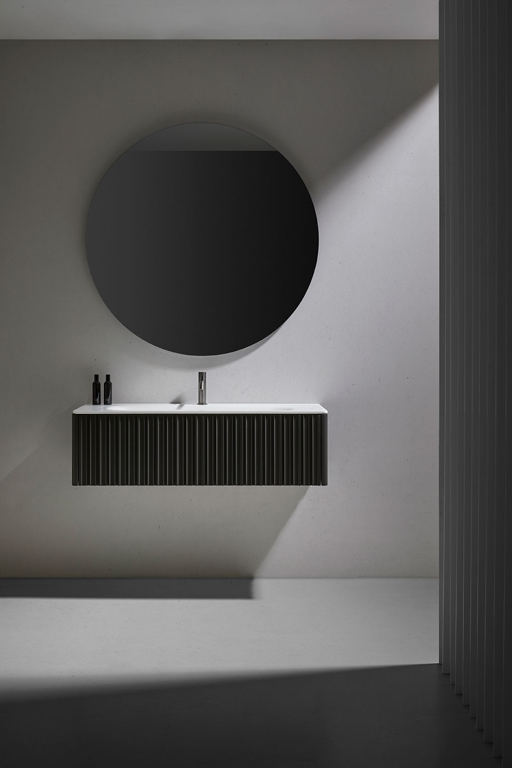 Mueble Bert flotante rectangular en color gris con parte superior en blanco. Espejo circular sobre el mueble y grifería en plata.