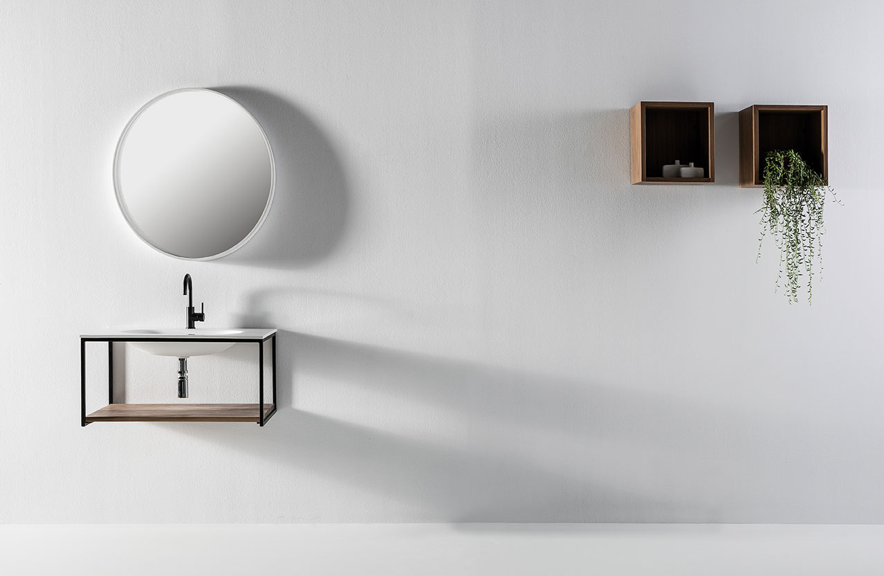 Mueble de baño Memphis minimalista parte superior en blanco y parte inferior en madera con grifo en negro. Espejo circular de baño y estanterías de madera en forma de cubo.